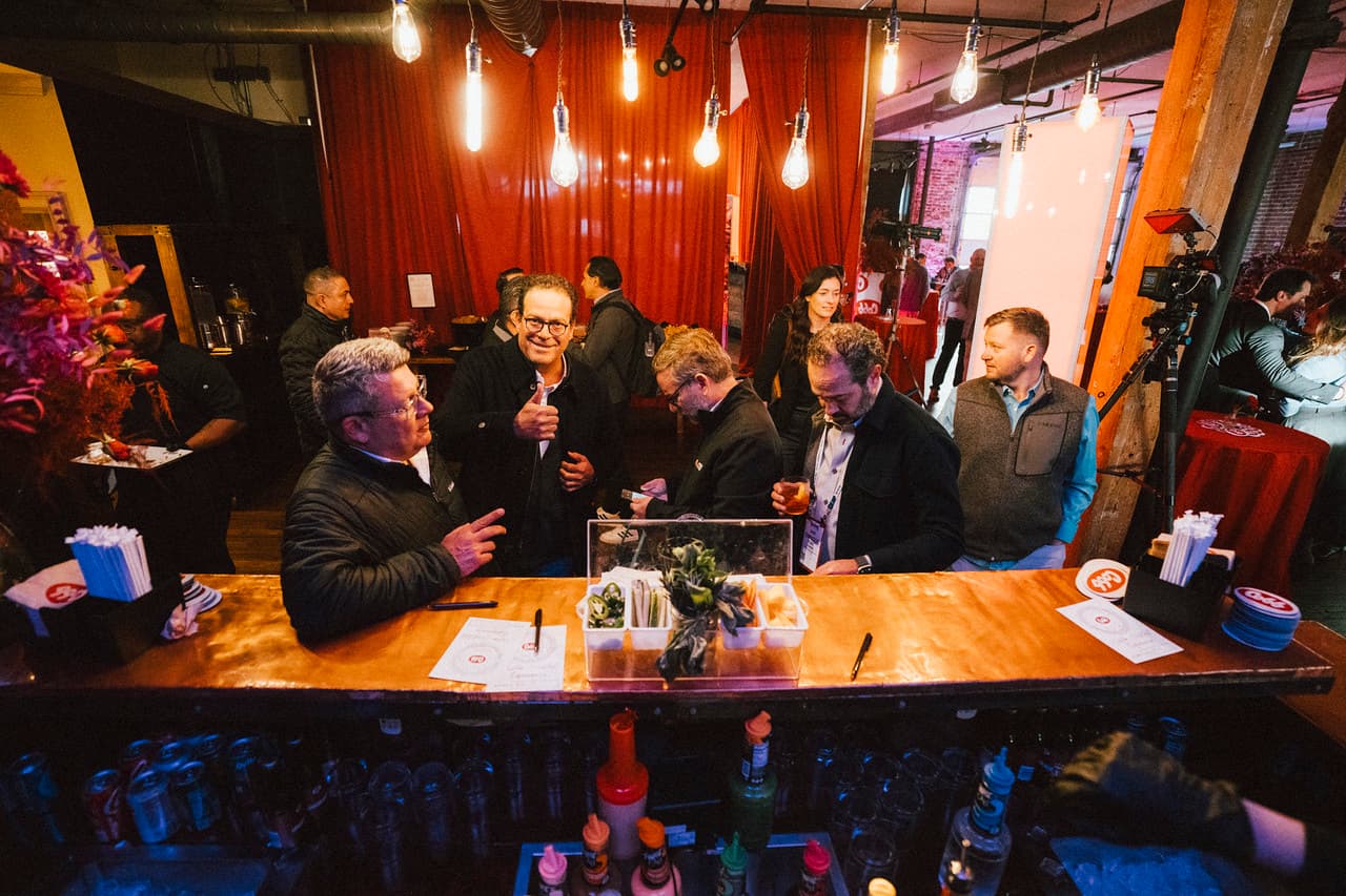 Guests mingling at copper-top bar under Edison bulbs and red drapes