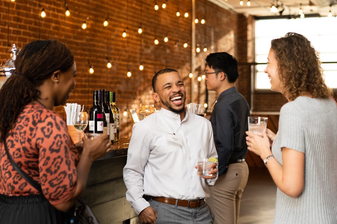 Colleagues laughing over drinks at the bar beneath string lights